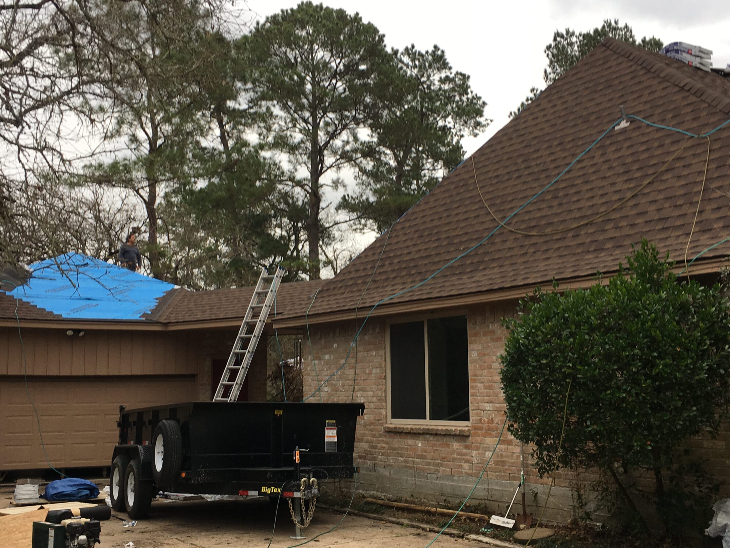 888c1971-14ab-4180-8cbd-e4e71a843339 Roof repair in progress on a residential house with trees in the background.