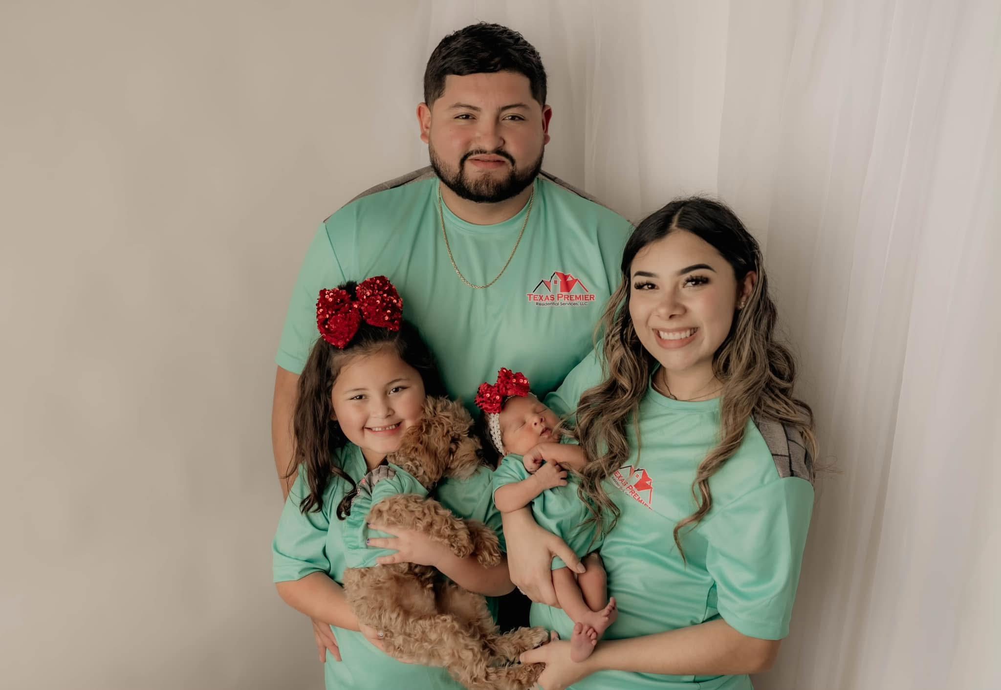 original-9E40EAC1-FB3D-437D-8E76-787A8499D380 Family of four wearing matching green outfits, smiling and holding a small dog.